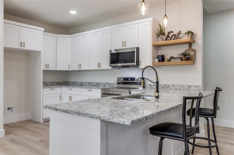 Kitchen featuring stainless steel appliances, kitchen peninsula, light wood-type flooring, and pendant lighting