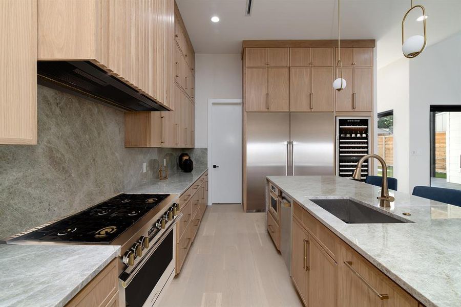 Kitchen with light stone countertops, high end appliances, sink, tasteful backsplash, and light brown cabinetry