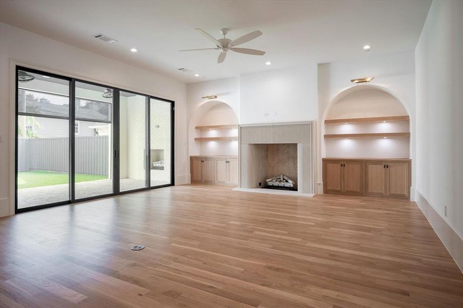 Unfurnished living room with built in shelves, ceiling fan, and light hardwood / wood-style floors