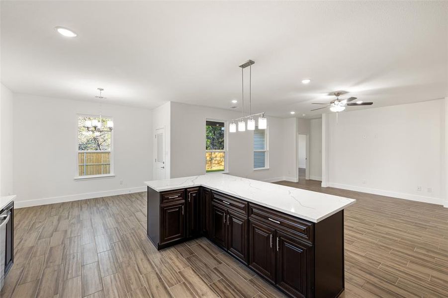 Kitchen with light hardwood / wood-style floors, ceiling fan with notable chandelier, dark brown cabinets, light stone countertops, and hanging light fixtures