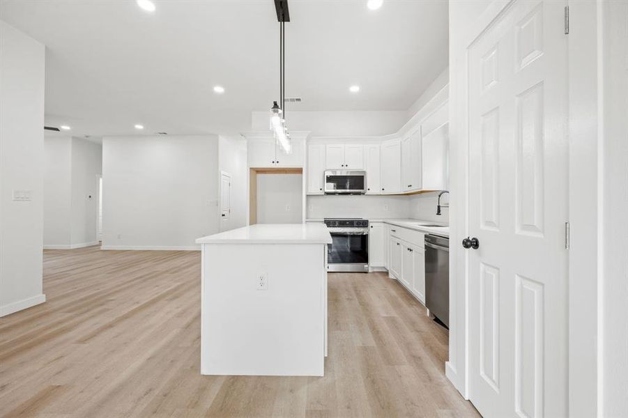 Kitchen featuring stainless steel appliances, white cabinets, decorative light fixtures, light hardwood / wood-style floors, and a kitchen island