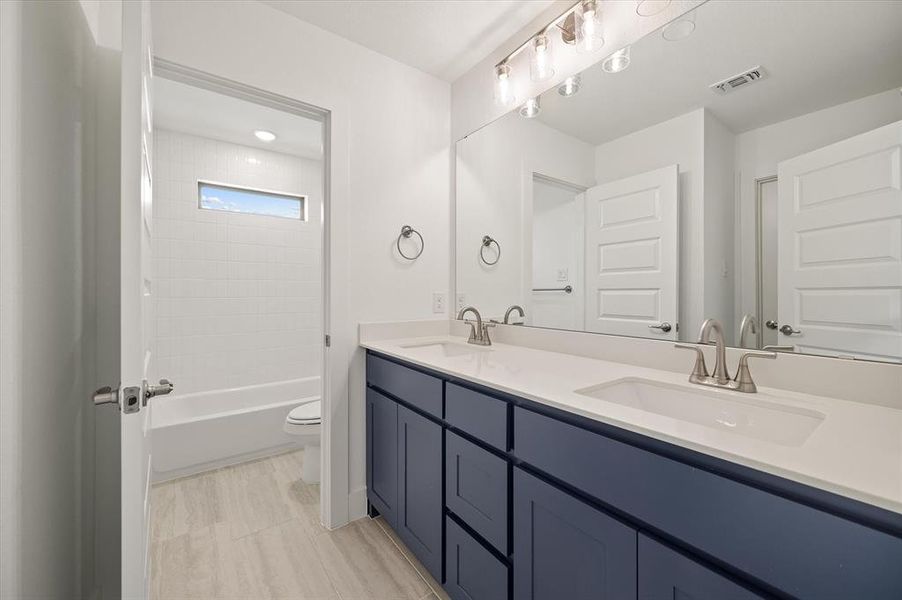 Full bathroom with tiled shower / bath combo, toilet, and dual bowl vanity