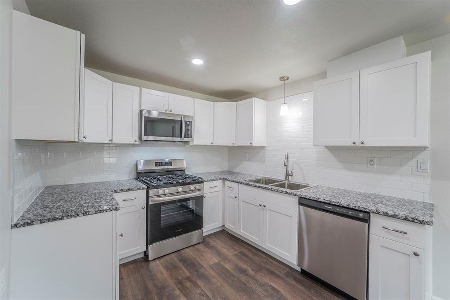 Kitchen with dark hardwood / wood-style floors, tasteful backsplash, stainless steel appliances, sink, and white cabinets