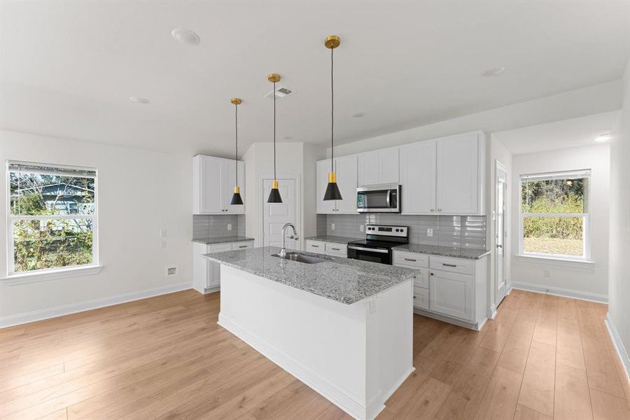 Kitchen featuring light stone counters, white cabinetry, light wood-type flooring, pendant lighting, and stainless steel appliances