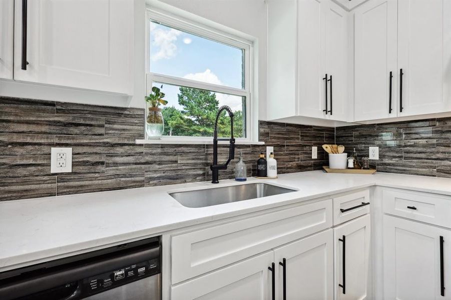 Kitchen with white cabinetry, dishwashing machine, tasteful backsplash, and sink