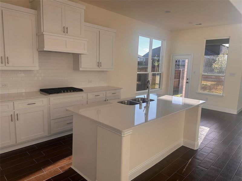 Kitchen featuring dark wood-type flooring, white cabinets, stainless steel gas cooktop, a kitchen island with sink, and sink