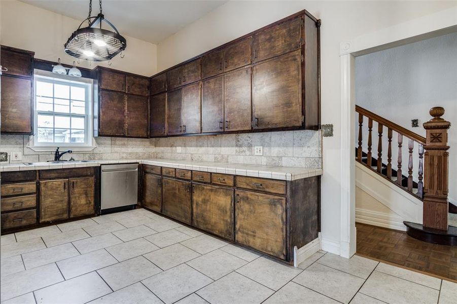 Kitchen featuring tasteful backsplash, light parquet floors, dark brown cabinetry, stainless steel dishwasher, and tile countertops