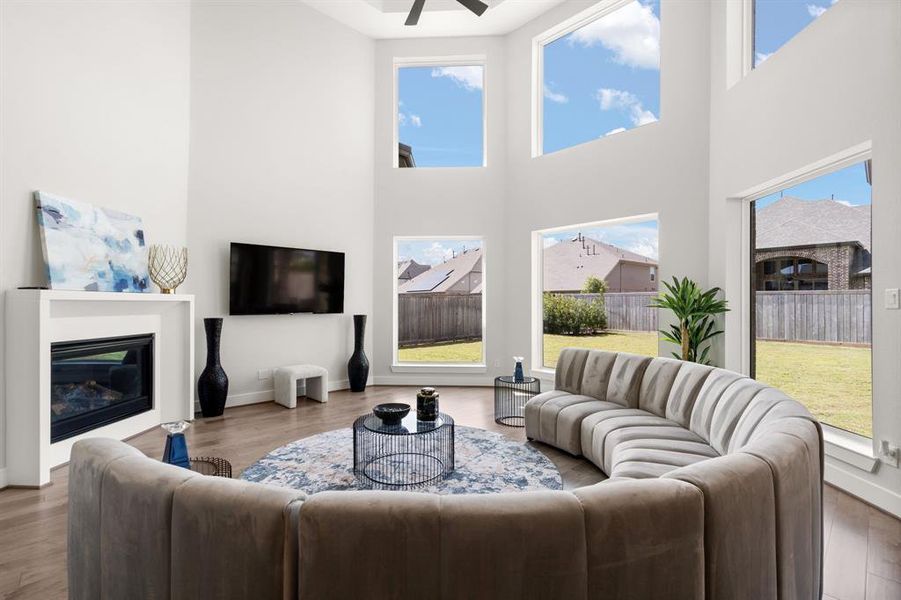 The living room is characterized by multiple large windows, tall ceilings with a ceiling fan, and a sleek fireplace, creating a bright and inviting atmosphere.