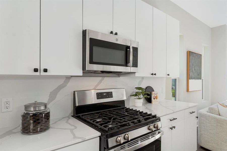 Kitchen featuring white cabinets, light stone counters, appliances with stainless steel finishes, and decorative backsplash