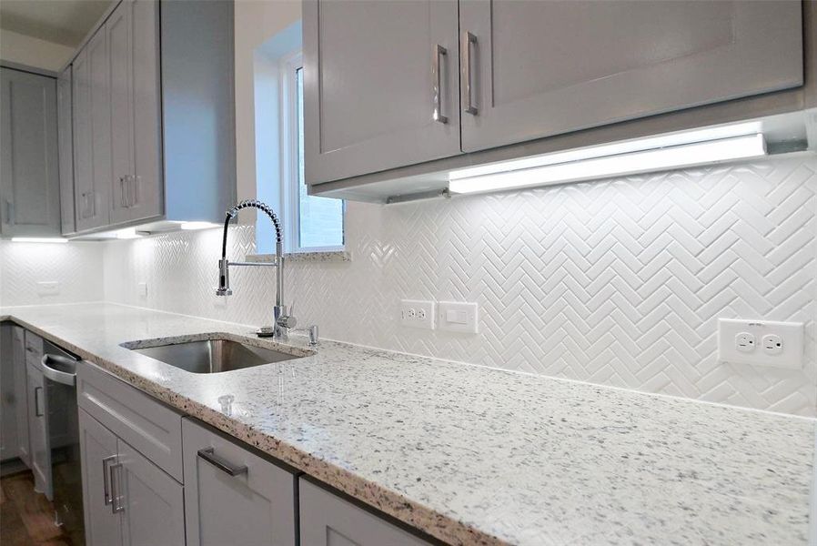 Kitchen with dishwasher, tasteful backsplash, sink, gray cabinetry, and light stone countertops