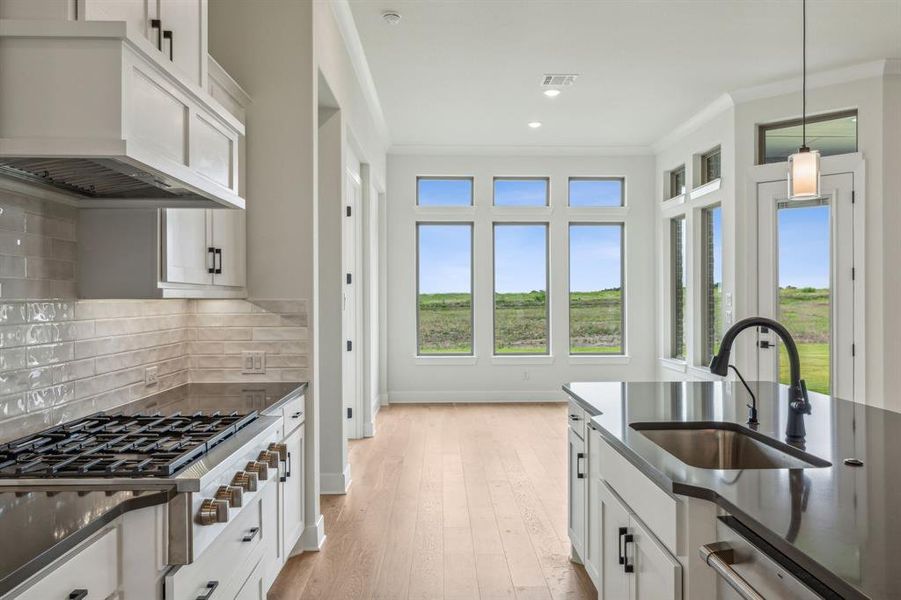 Kitchen featuring decorative light fixtures, white cabinets, custom range hood, and sink