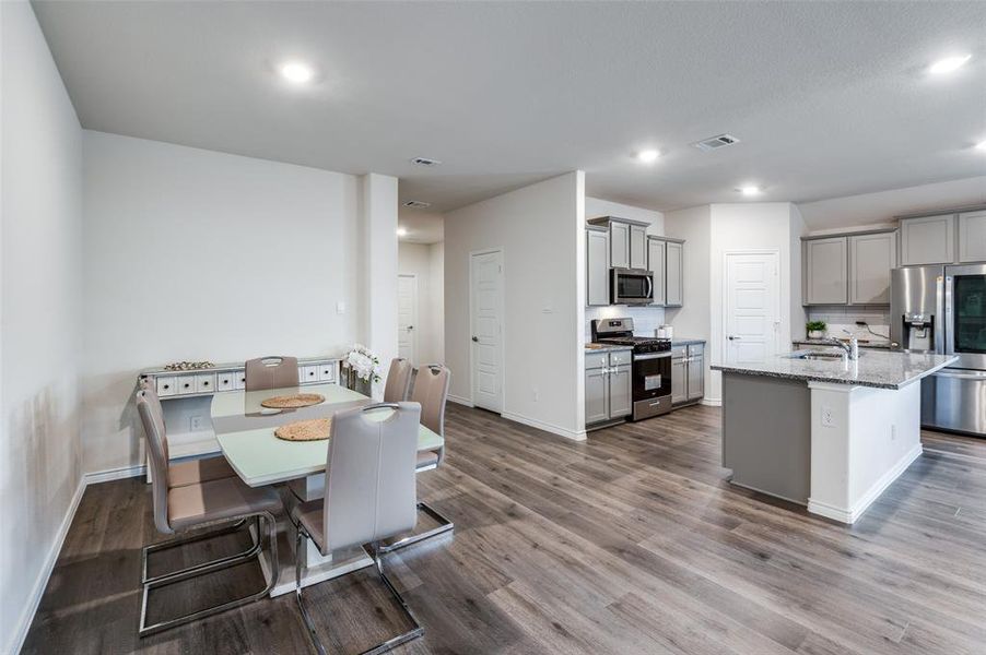 Kitchen featuring light stone countertops, appliances with stainless steel finishes, an island with sink, dark hardwood / wood-style flooring, and gray cabinets