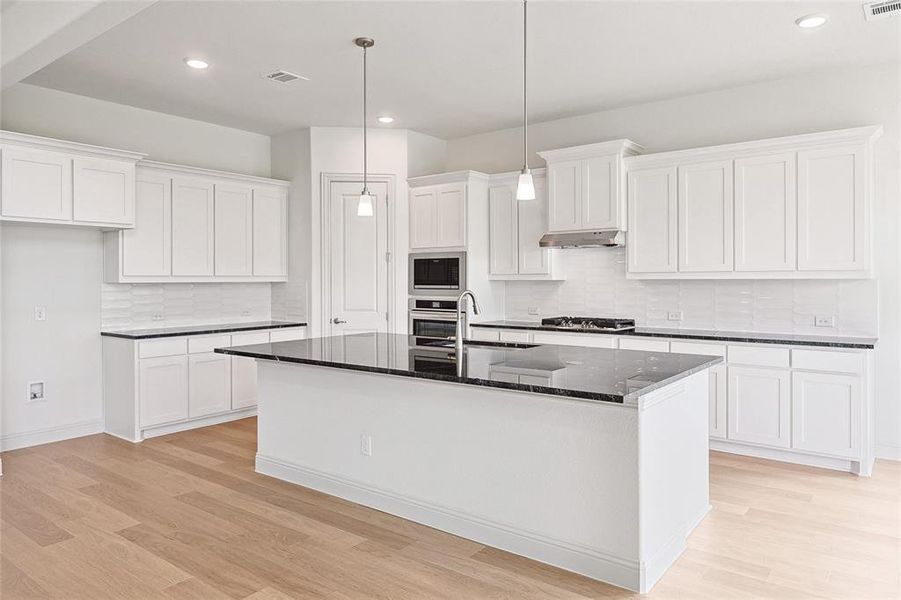 Kitchen with tasteful backsplash, stainless steel appliances, a center island with sink, light wood-type flooring, and sink