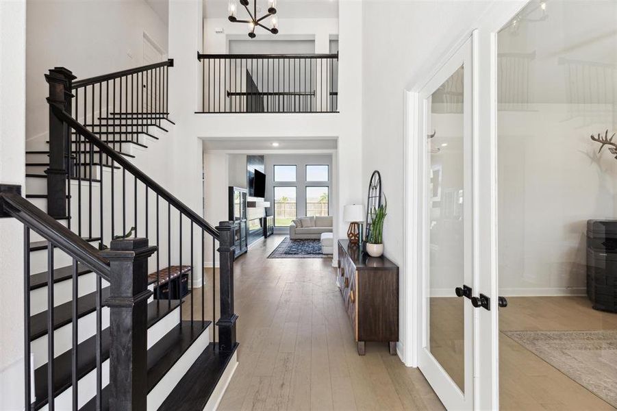 This photo showcases a spacious and modern entryway with a striking black staircase leading to a second level, complemented by high ceilings and natural light flowing from large rear windows. The entry opens to a bright living area, offering a seamless flow for entertaining and comfortable living.