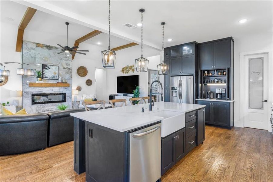 Kitchen with sink, a stone fireplace, a center island with sink, appliances with stainless steel finishes, and light wood-type flooring