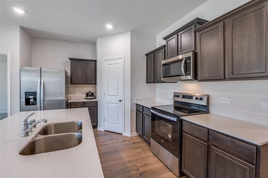 Kitchen featuring appliances with stainless steel finishes, dark brown cabinetry, sink, and dark hardwood / wood-style flooring