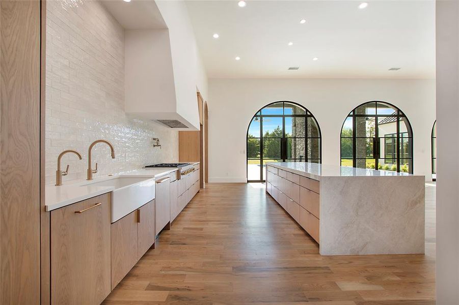 Kitchen featuring sink, light hardwood / wood-style floors, a spacious island, custom exhaust hood, and backsplash