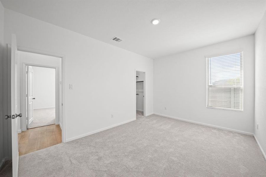 Bedroom with neutral walls and carpet flooring, featuring a window with blinds and two doorways, across from the other bedroom