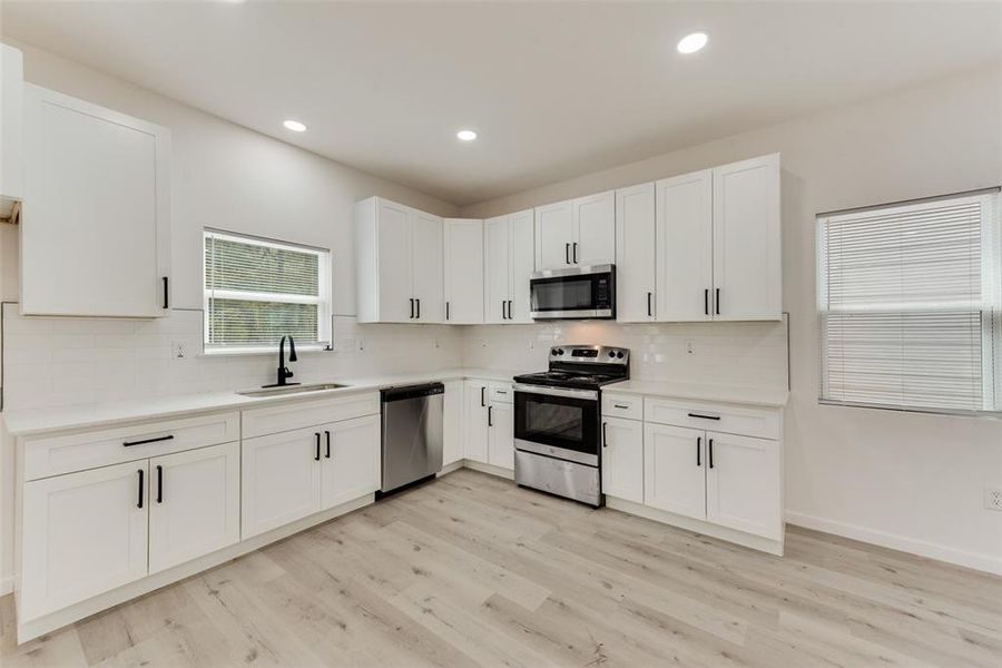 Kitchen featuring stainless steel appliances, light hardwood / wood-style floors, white cabinetry, sink, and tasteful backsplash