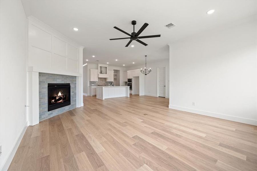 Unfurnished living room with sink, a tiled fireplace, ceiling fan with notable chandelier, and light hardwood / wood-style floors