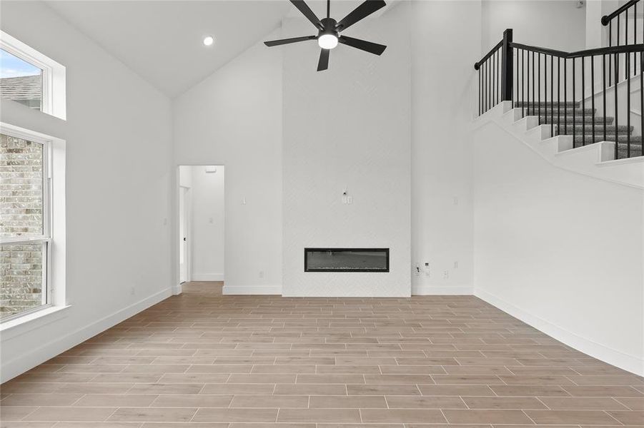 Unfurnished living room with ceiling fan, high vaulted ceiling, and light wood-type flooring