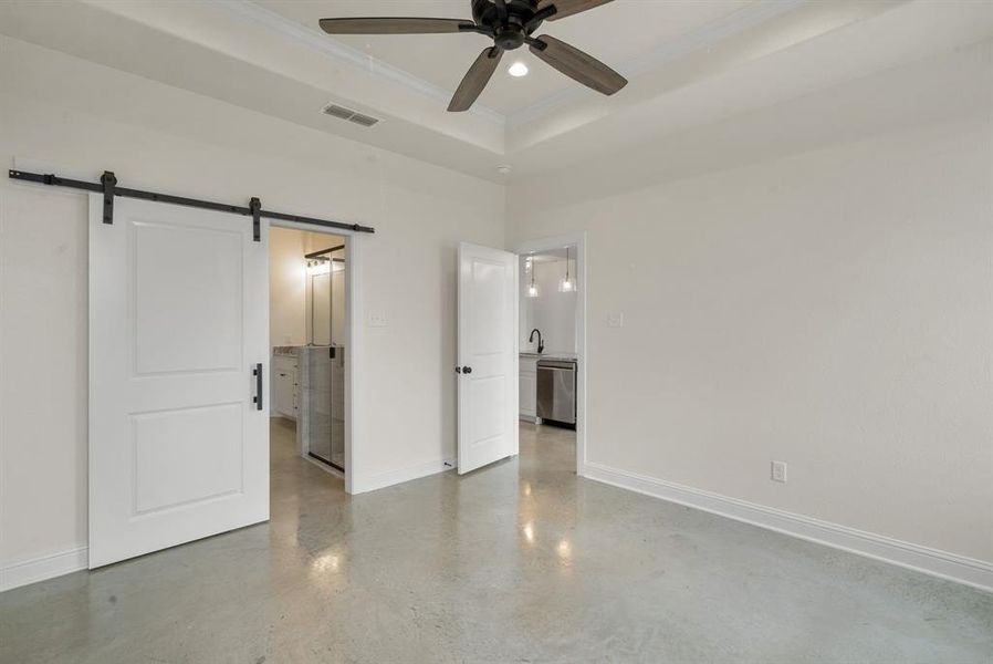 Unfurnished bedroom featuring a barn door, ensuite bathroom, ornamental molding, ceiling fan, and a raised ceiling