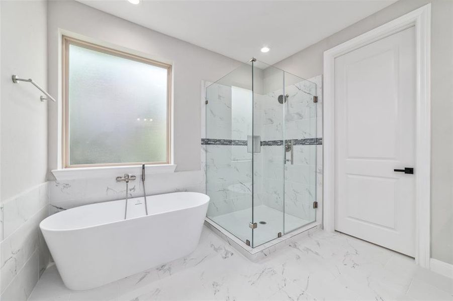 Enjoy the elegance of the primary bathroom, featuring a sleek ceramic-tiled floor, a luxurious freestanding tub, and a spacious glass-enclosed shower.