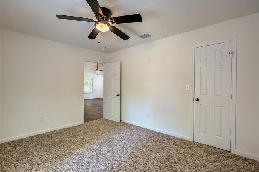 Third room with ceiling fan and dark carpet