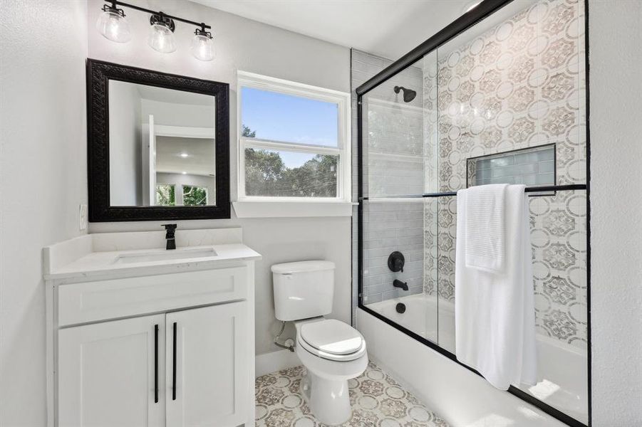 Full bathroom featuring vanity, toilet, tile patterned floors, and bath / shower combo with glass door