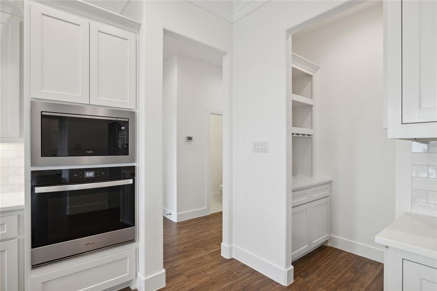 Kitchen featuring dark wood-type flooring, white cabinets, appliances with stainless steel finishes, and tasteful backsplash