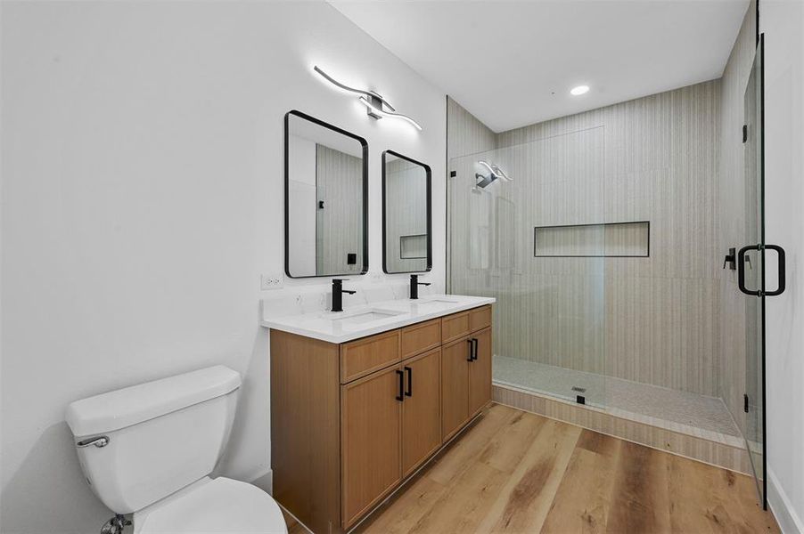 Bathroom with dual bowl vanity, an enclosed shower, hardwood / wood-style flooring, and toilet