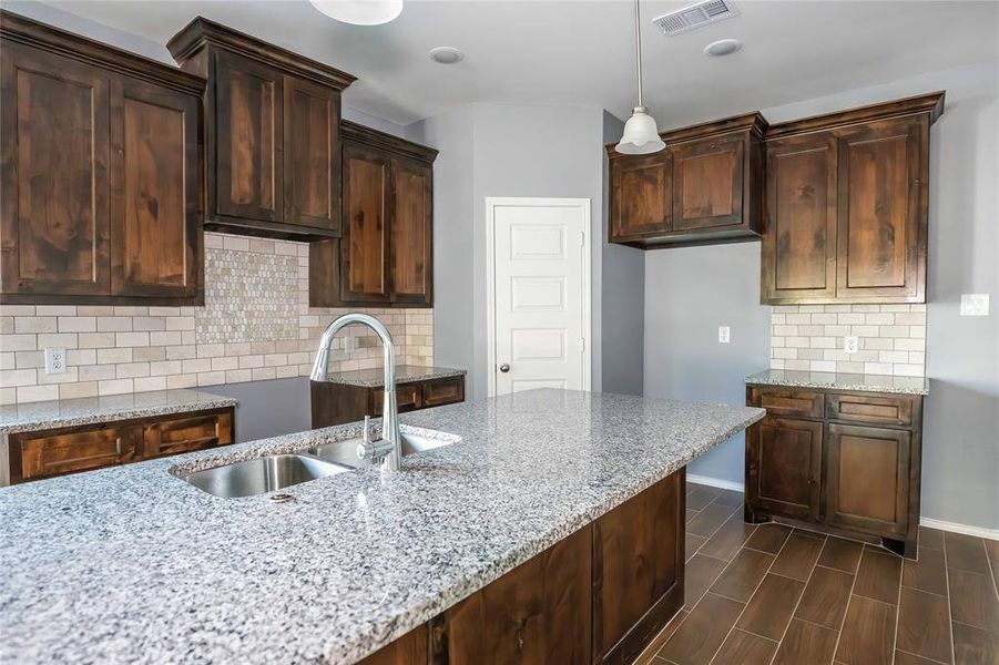 Kitchen featuring light stone countertops, hanging light fixtures, sink, and tasteful backsplash