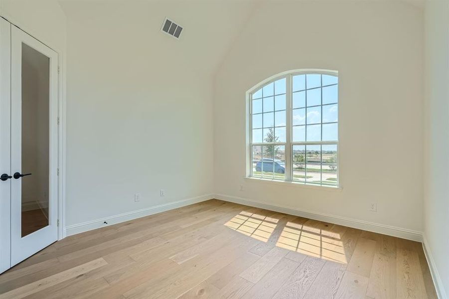 Spare room with light hardwood / wood-style floors, french doors, and high vaulted ceiling