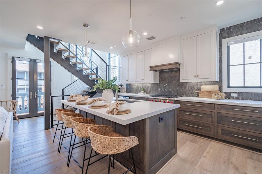 Kitchen featuring hanging light fixtures, quartz countertops, a kitchen island with sink, and light hardwood floors