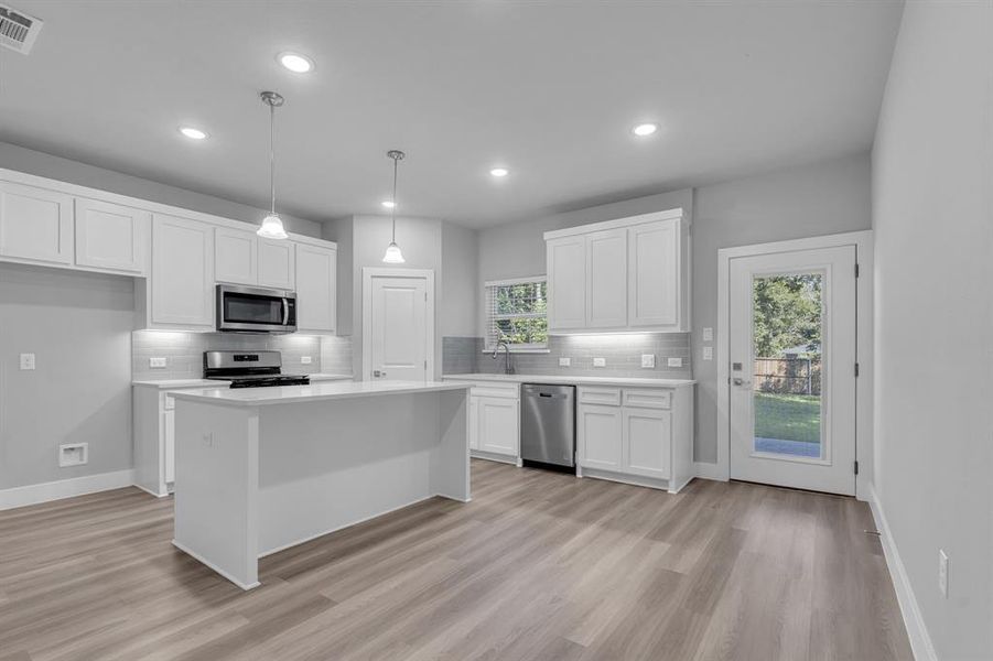 Kitchen featuring appliances with stainless steel finishes, hanging light fixtures, light hardwood / wood-style floors, and white cabinets