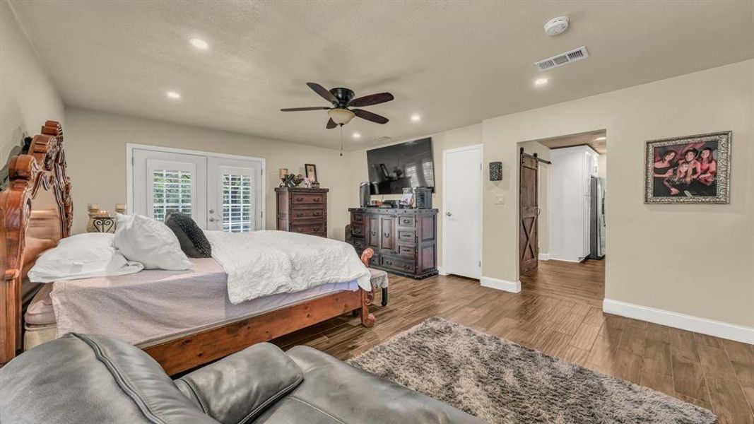 Bedroom featuring stainless steel fridge, hardwood / wood-style floors, ceiling fan, access to outside, and a barn door