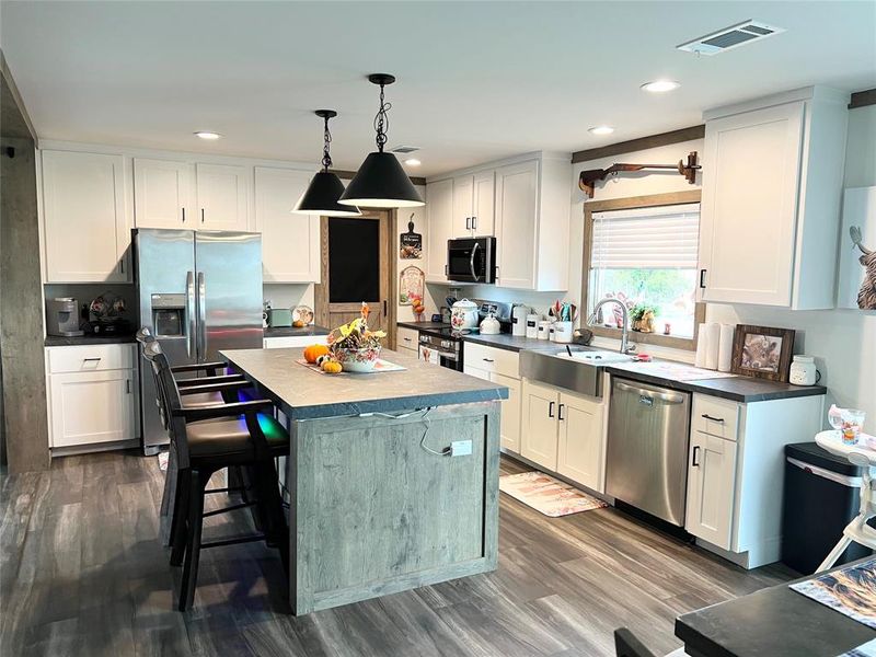 Kitchen with a kitchen island, white cabinetry, sink, decorative light fixtures, and stainless steel appliances