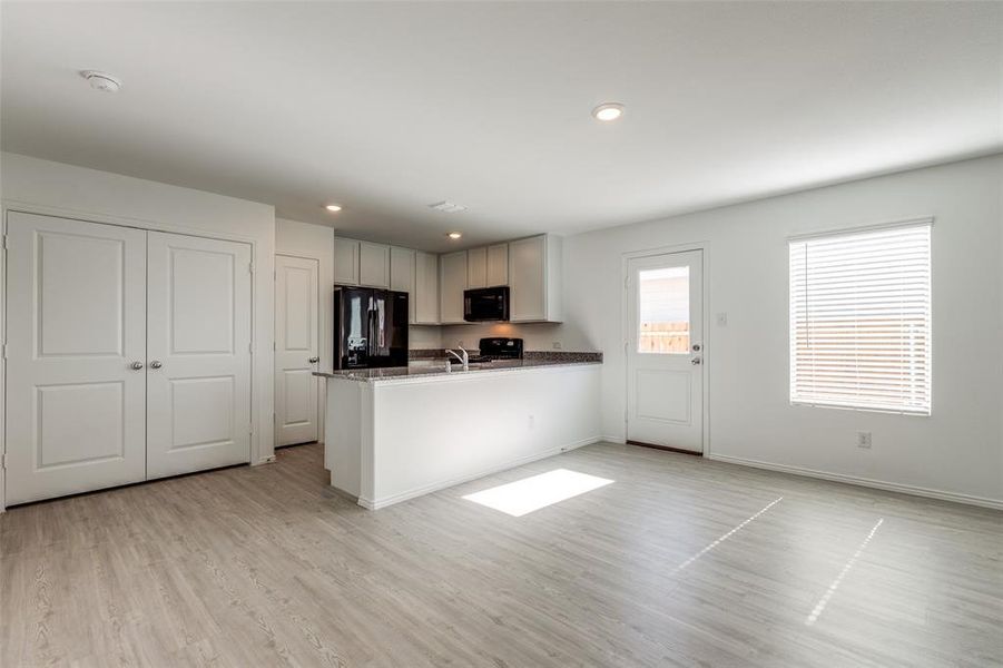 Kitchen with dark stone counters, black appliances, sink, light hardwood / wood-style floors, and kitchen peninsula