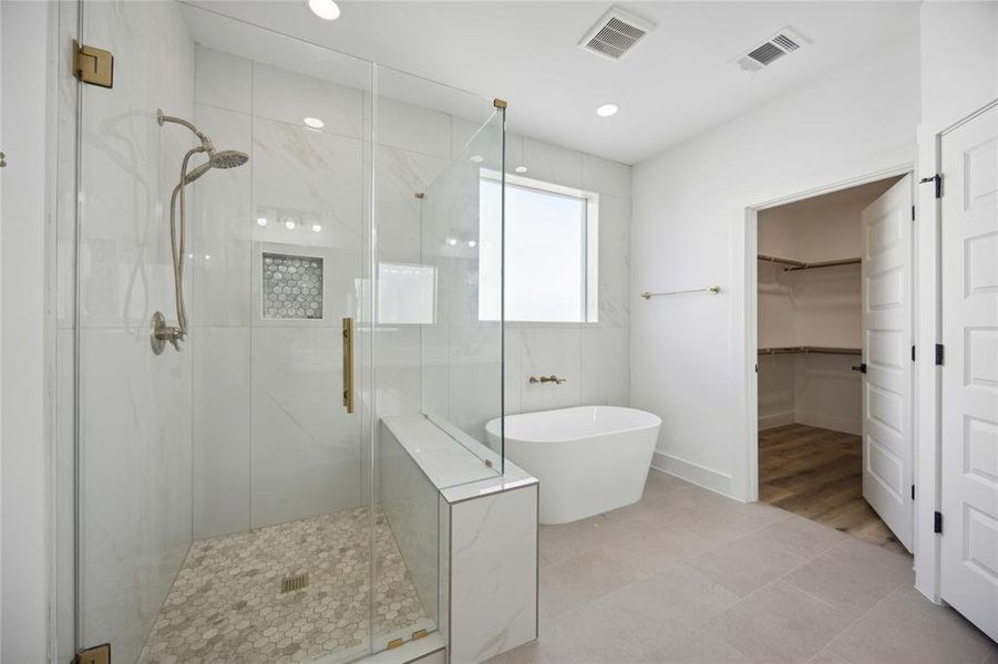 The modern primary bathroom features a glass-enclosed walk-in shower, a freestanding soaking tub, and a walk-in closet. The space is finished with neutral colors, offering a sleek and clean design.