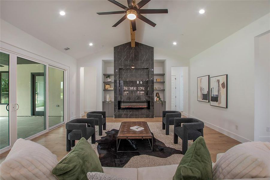 Living room featuring lofted ceiling with beams, ceiling fan, a tiled fireplace, and hardwood / wood-style flooring