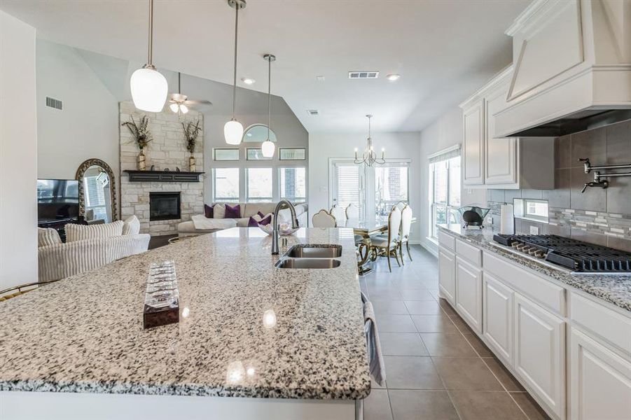 Kitchen featuring custom range hood, white cabinets, stainless steel gas cooktop, a stone fireplace, and sink