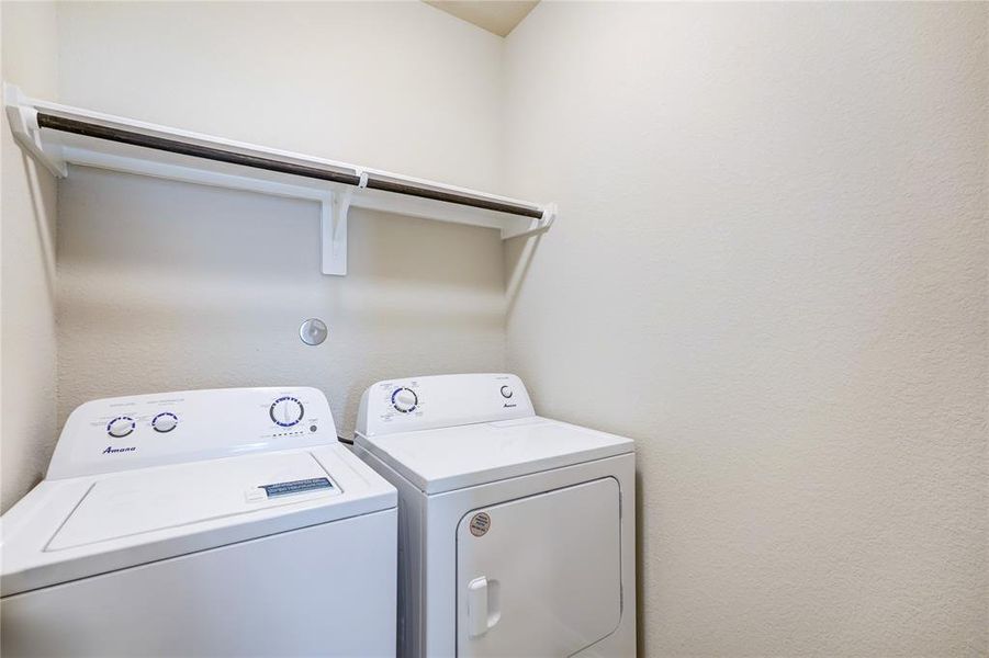This laundry space features a pristine white washer and dryer set, complemented by a handy storage shelf above for laundry essentials. The area is meticulously maintained and well-lit, ensuring both functionality and a clean appearance.