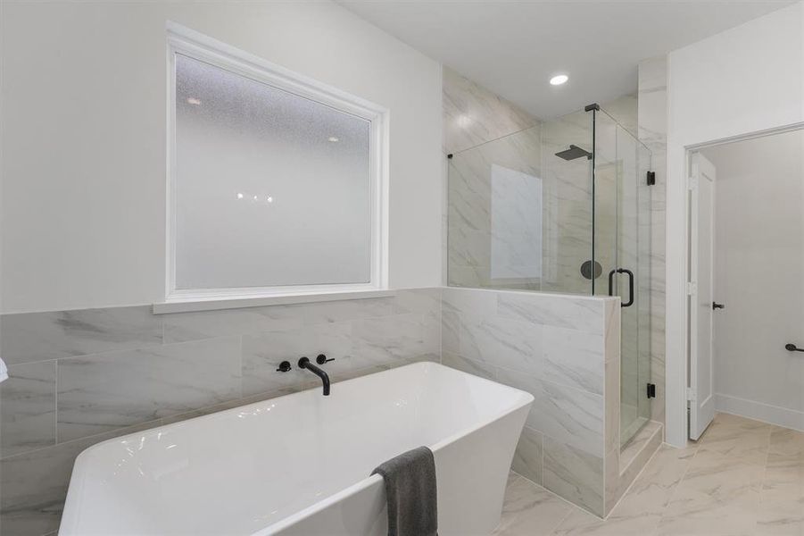 Relax in your modern bathroom with a stand alone deep soaking tub surrounded by stone tiles, frameless stand alone shower, large window providing natural light.