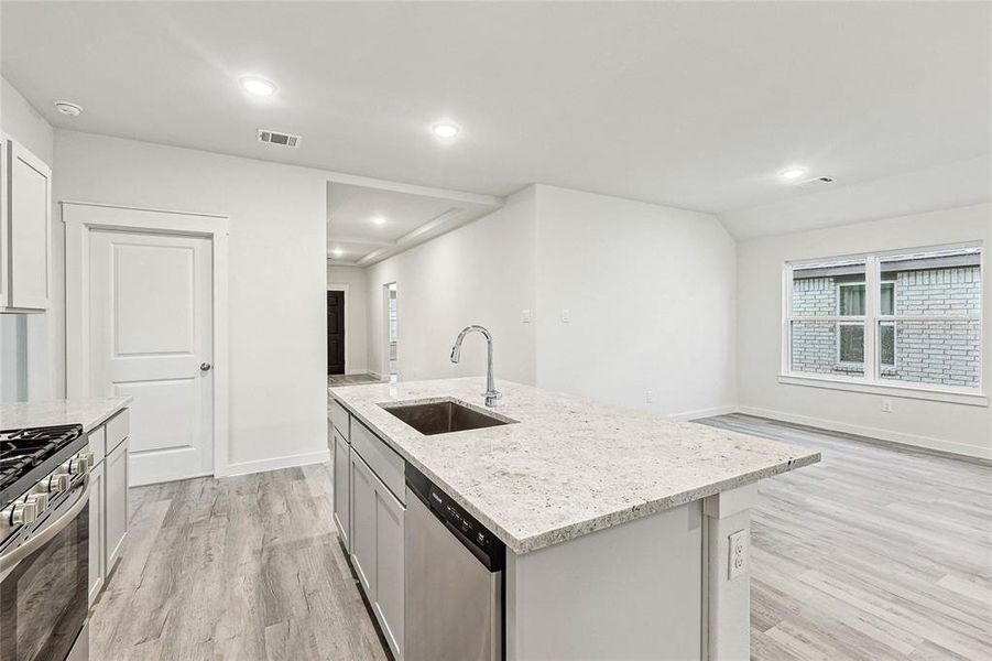 Kitchen with light wood-type flooring, light stone counters, an island with sink, stainless steel appliances, and sink