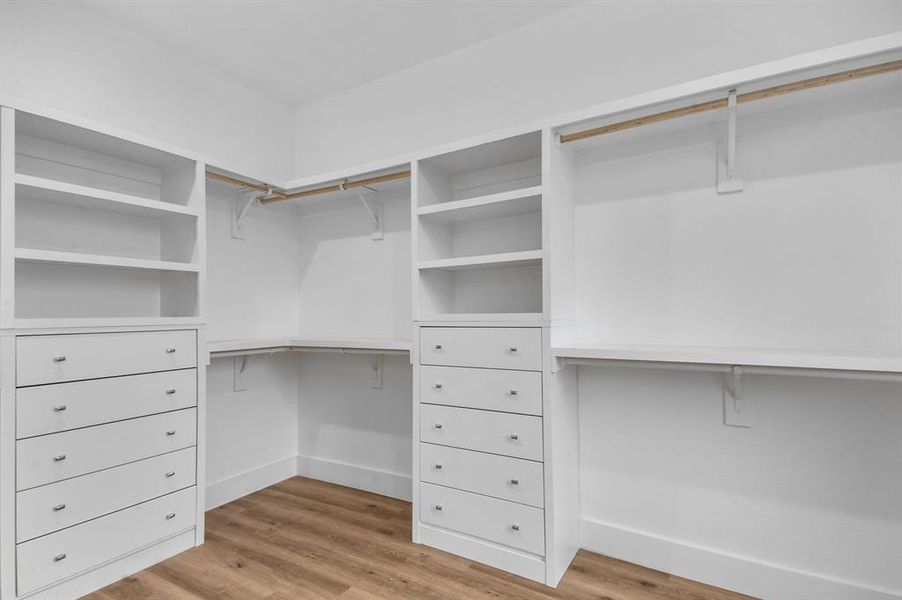 Walk in closet with light hardwood / wood-style floors