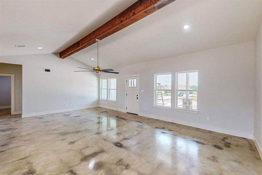 Unfurnished living room featuring concrete floors, a healthy amount of sunlight, vaulted ceiling with beams, and ceiling fan