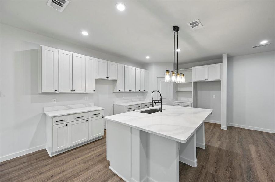 Kitchen featuring hanging light fixtures, sink, an island with sink, and white cabinets