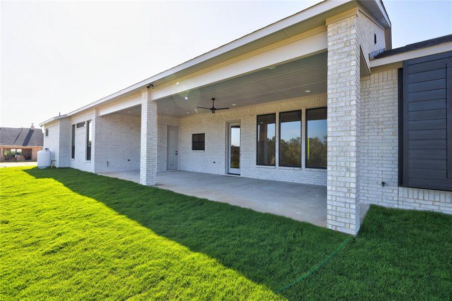 Rear view of house featuring ceiling fan, a lawn, and a patio area