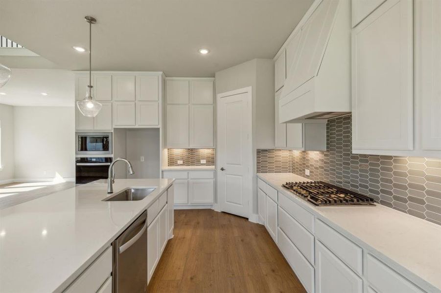 Kitchen with light hardwood / wood-style floors, sink, appliances with stainless steel finishes, hanging light fixtures, and white cabinets