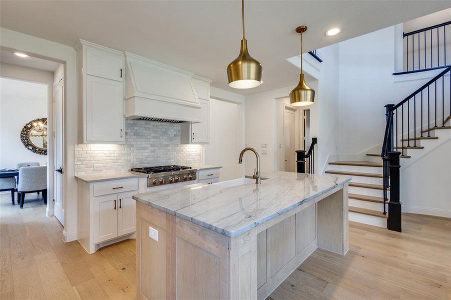 Kitchen with a kitchen island with sink, light hardwood / wood-style flooring, premium range hood, and white cabinetry